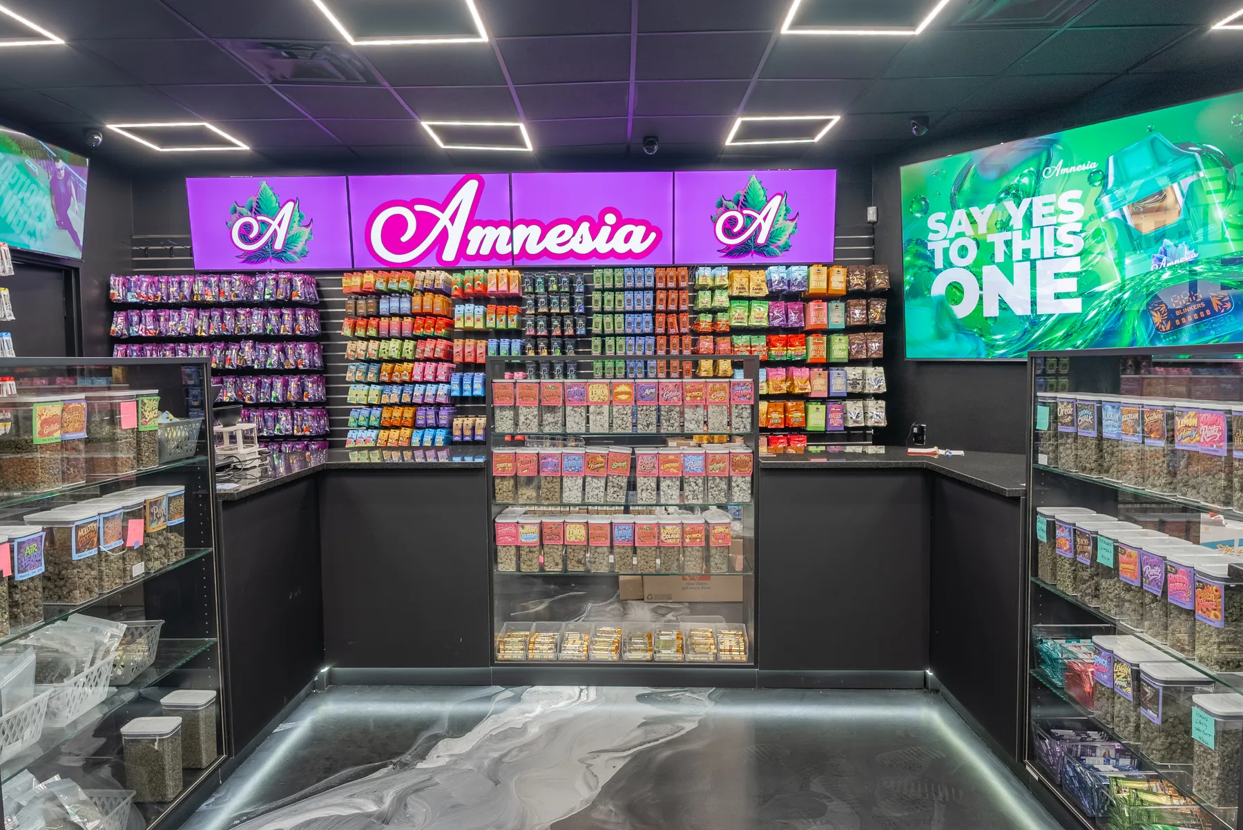 A stocked GreenCare cannabis wall with colorful product displays and digital signage.